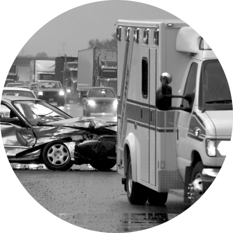 Black and white photograph of a highway collision scene depicting a wrecked car and an ambulance, under stormy conditions with blurred trucks in the background.