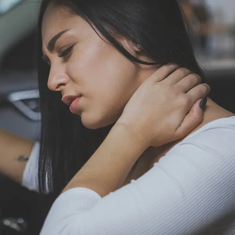 A woman experiencing neck pain from an auto accident, holding her neck with a pained expression, sitting inside a car.