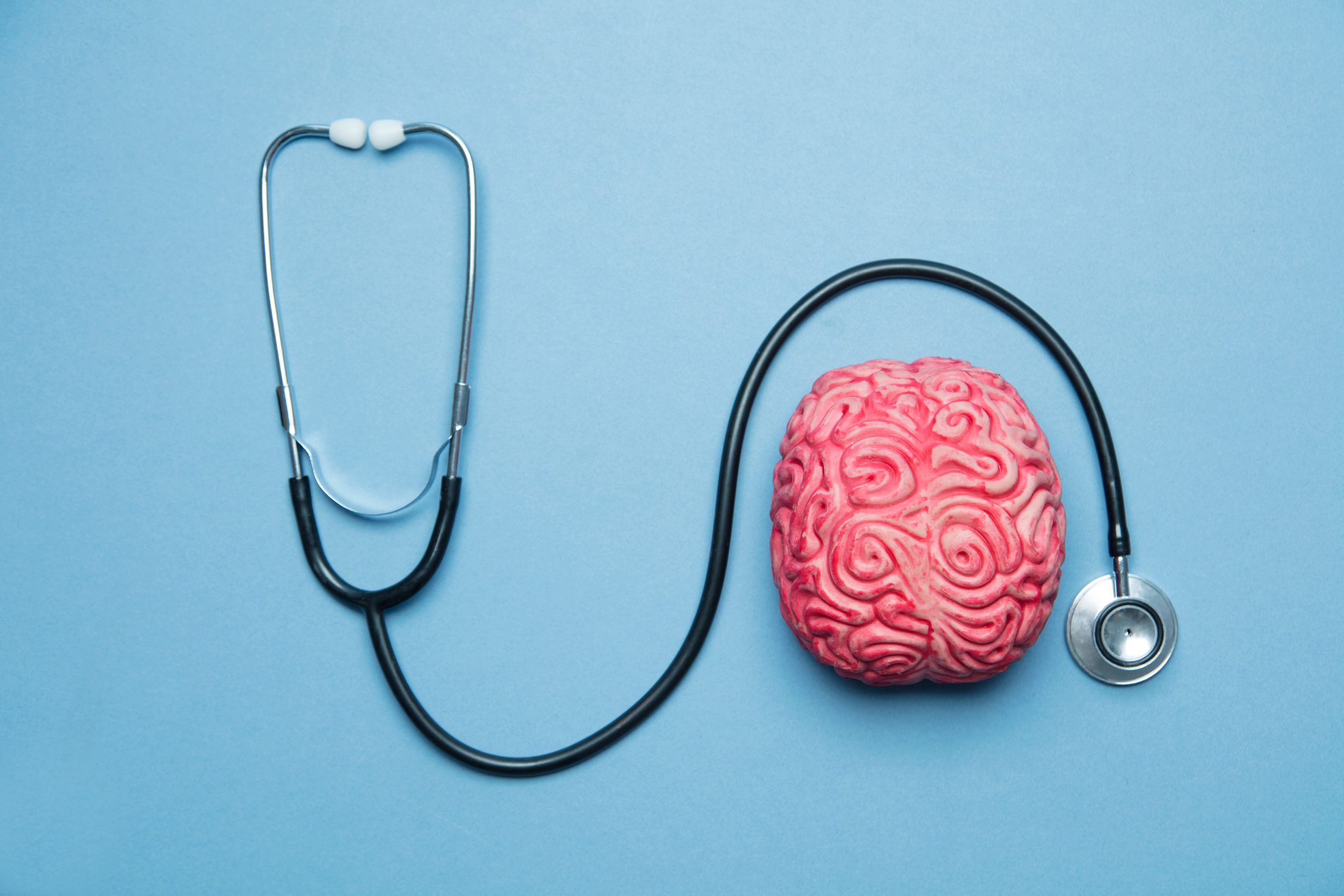 A stethoscope encircles a realistic model of a human brain on a solid blue background, symbolizing mental health examination post-auto accidents.