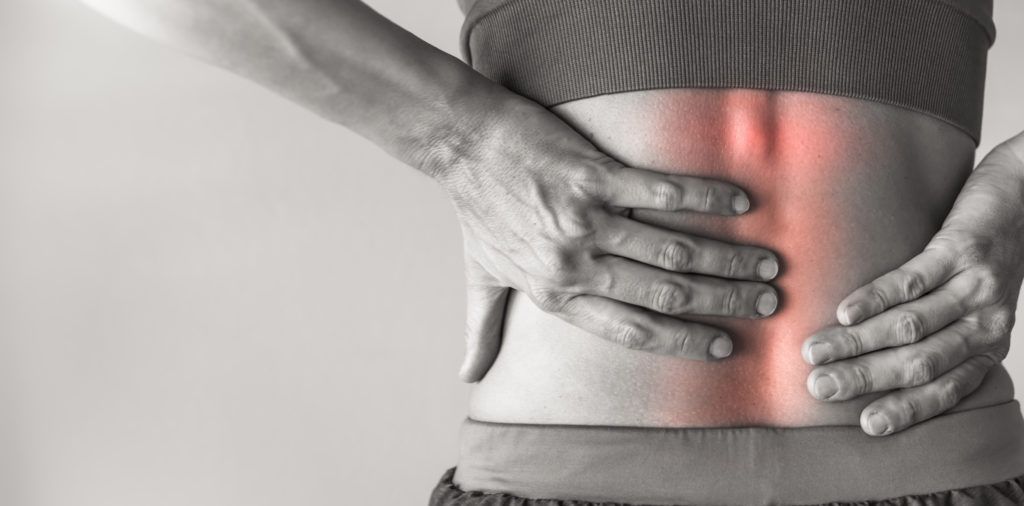 A person holding their lower back, displaying visible back pain highlighted by a red glow on the skin, suggesting acute backache or injury. Only the torso and hands are shown against a gray background.