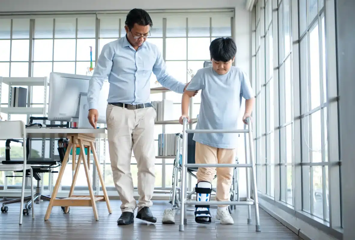 Physical therapist assisting a child with a leg brace using a walker during personalized rehabilitation after an injury.