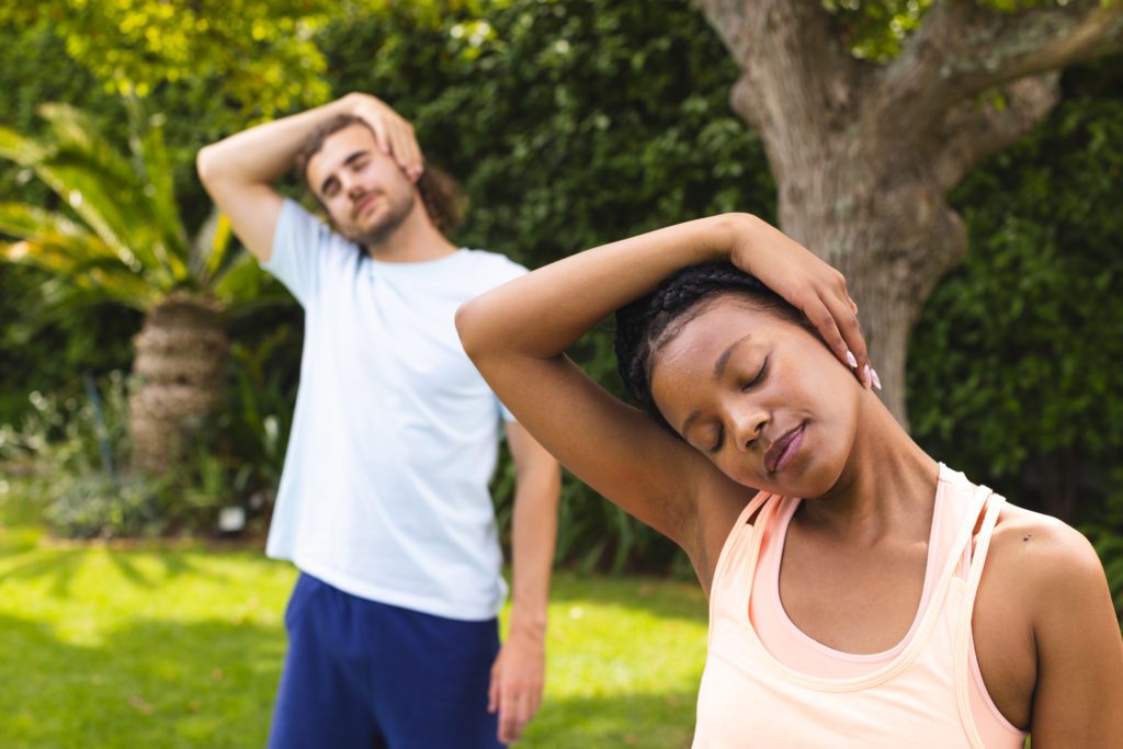 man and woman doing neck stretches in the park.