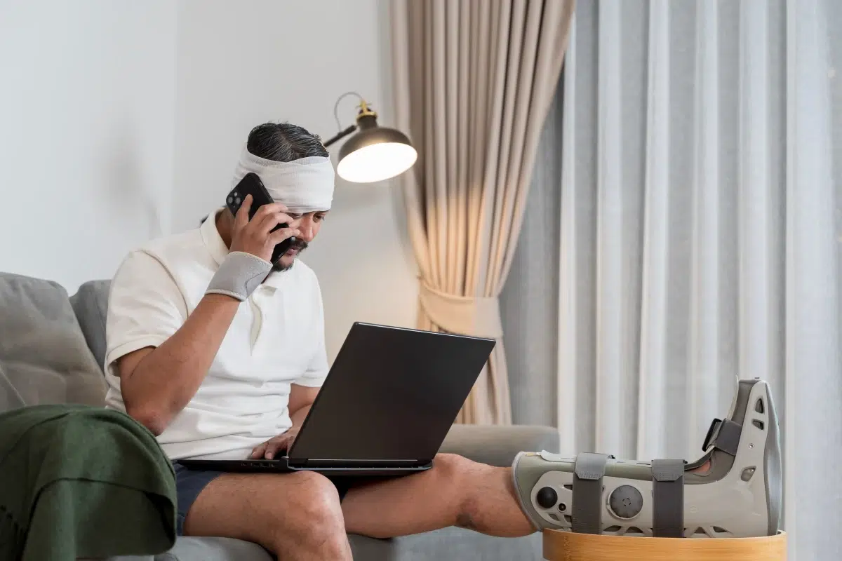 Man with leg brace and head injury working on a laptop at home, representing car crash recovery, mental health after car accident, and auto accident recovery in Florida.