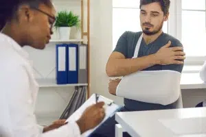 Patient with arm in a sling speaking with a medical professional, representing car accident injury treatment, car accident rehabilitation, and recovery after a car crash.