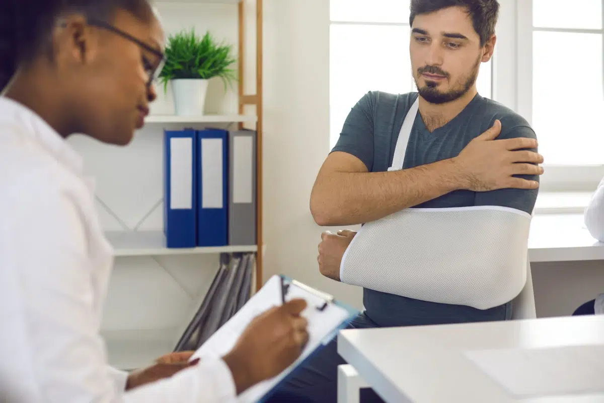 Patient with arm in a sling speaking with a medical professional, representing car accident injury treatment, car accident rehabilitation, and recovery after a car crash.