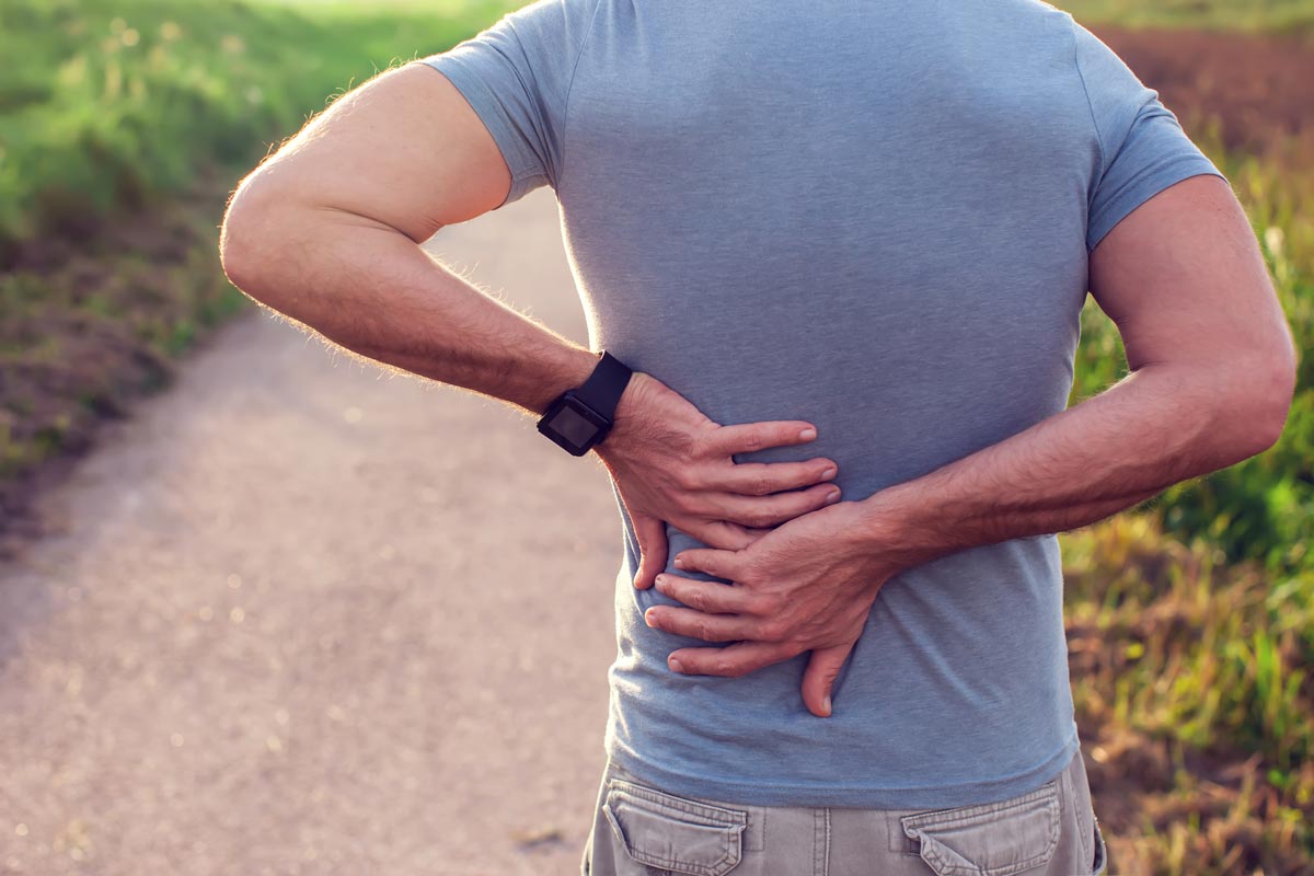 Man holding his lower back outdoors, illustrating chronic back pain and common causes of spinal discomfort