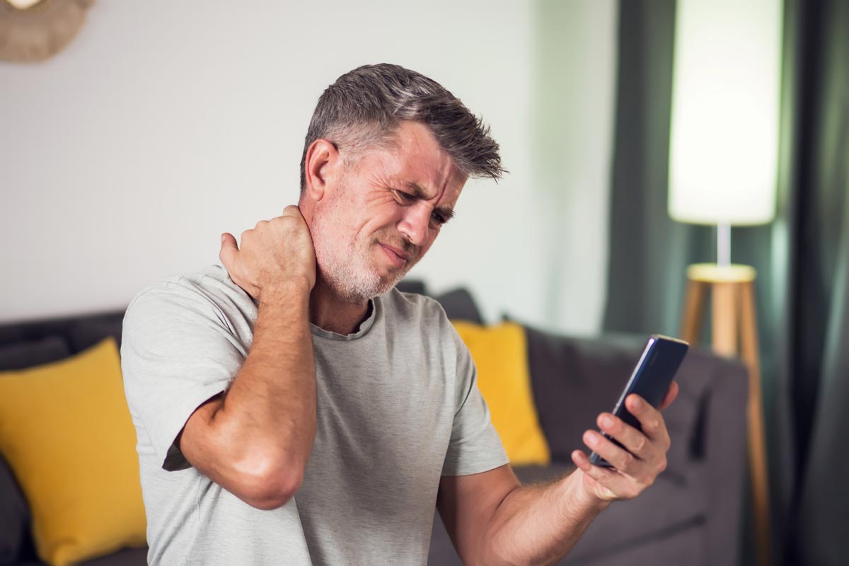 Man holding his neck while looking at a smartphone, illustrating tech neck and spine strain caused by prolonged device use