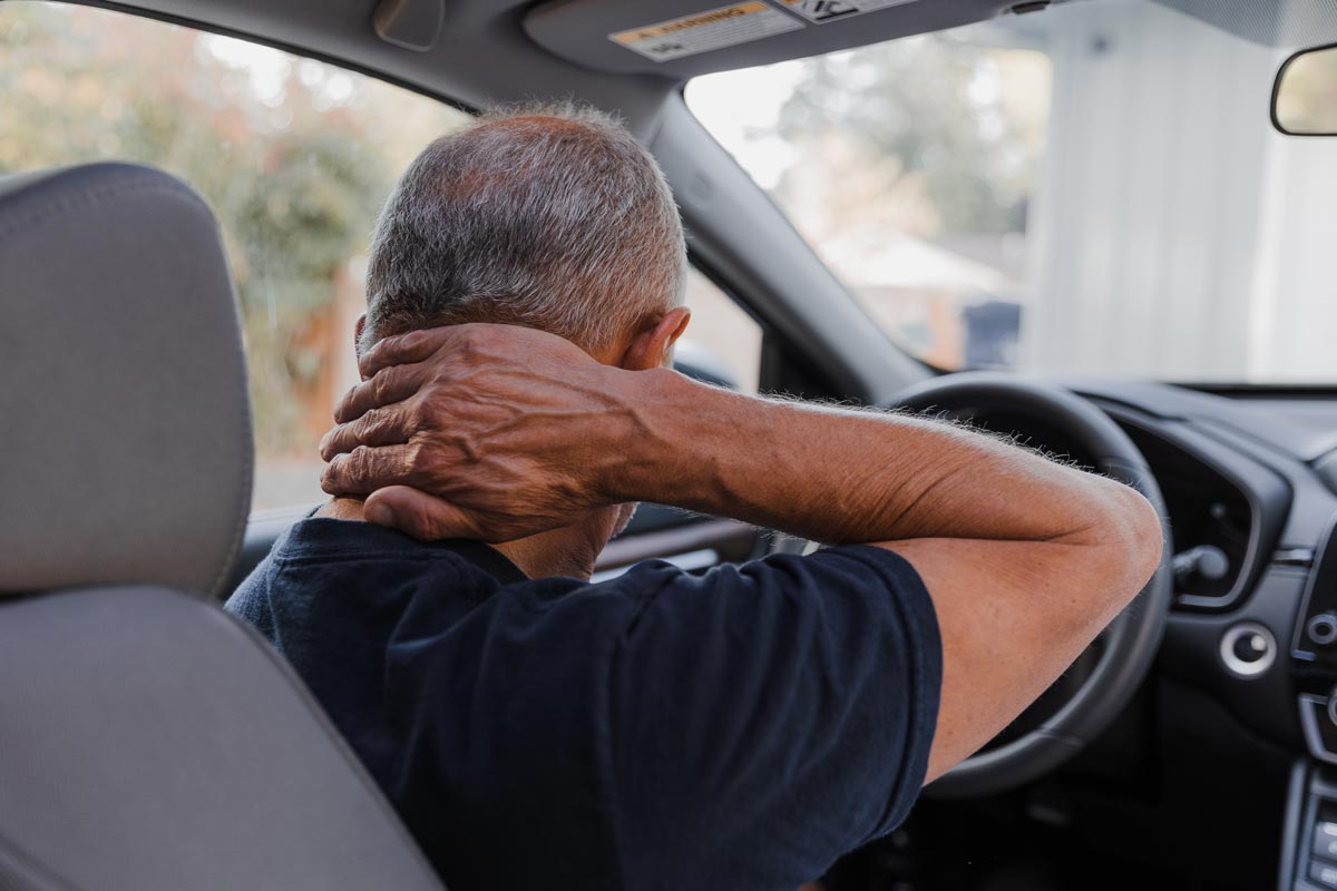 Man holding his neck while sitting in a car, illustrating whiplash and neck pain after a car accident